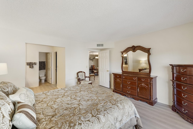 bedroom featuring a textured ceiling, light hardwood / wood-style flooring, and ensuite bath