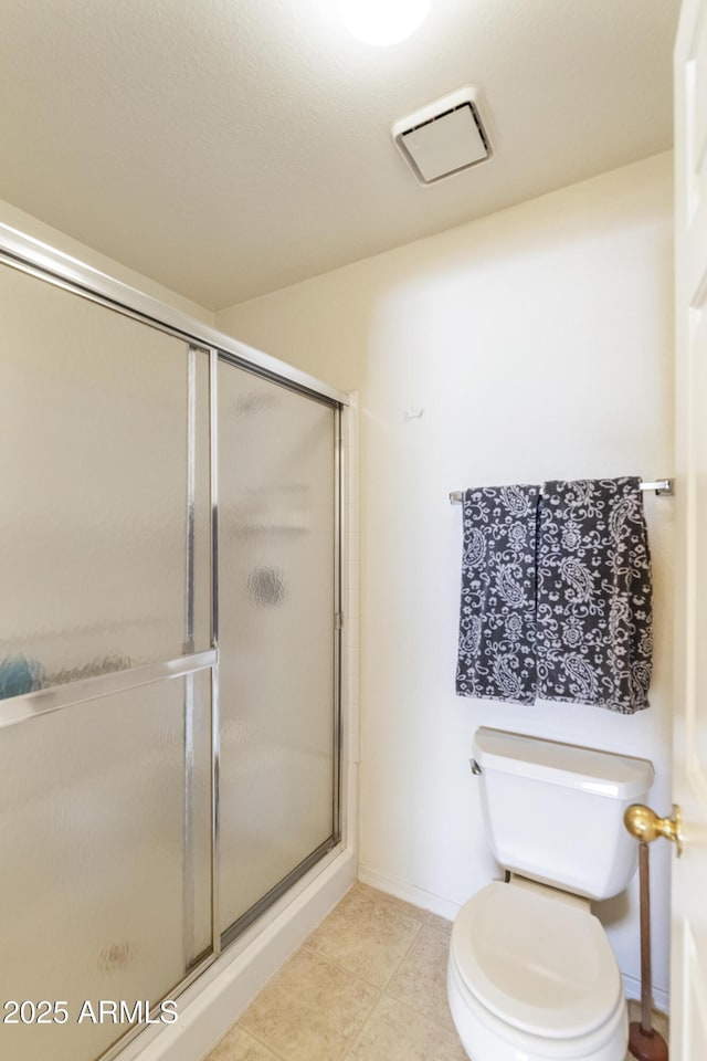 bathroom featuring toilet, tile patterned flooring, and a shower with shower door