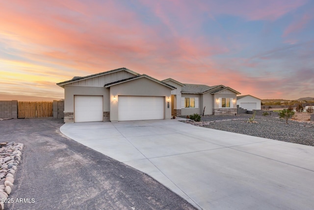 ranch-style house with a garage, fence, stone siding, driveway, and board and batten siding