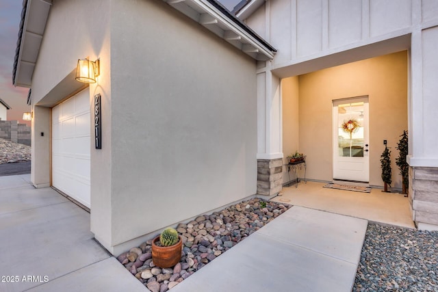 view of exterior entry featuring a garage, board and batten siding, and stucco siding