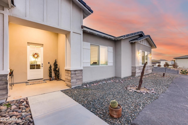 view of exterior entry with stone siding, board and batten siding, a patio area, and stucco siding