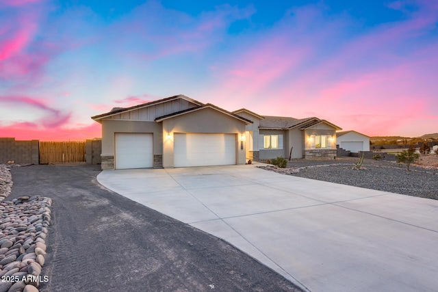 ranch-style house with an attached garage, fence, concrete driveway, stone siding, and stucco siding