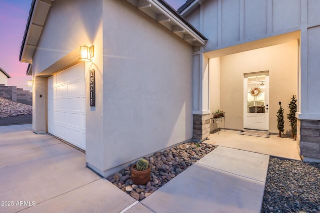 view of exterior entry featuring a garage, board and batten siding, and stucco siding