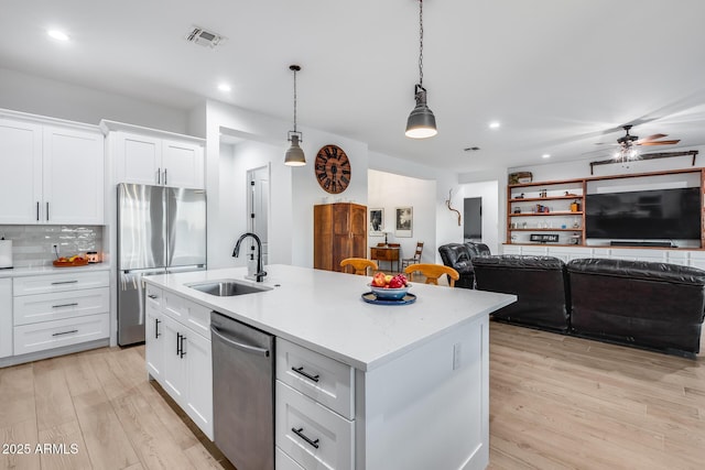 kitchen featuring open floor plan, hanging light fixtures, stainless steel appliances, white cabinetry, and a sink