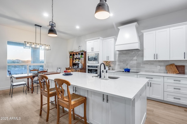 kitchen featuring stainless steel appliances, premium range hood, white cabinetry, and pendant lighting