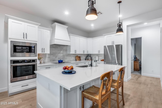 kitchen featuring stainless steel appliances, custom exhaust hood, a kitchen island with sink, and white cabinets