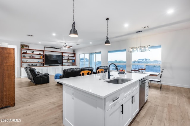 kitchen featuring a sink, open floor plan, light countertops, hanging light fixtures, and an island with sink