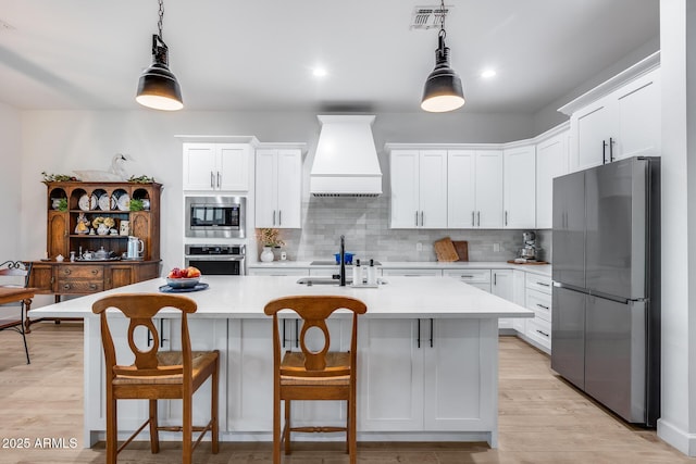 kitchen with stainless steel appliances, white cabinetry, hanging light fixtures, light countertops, and custom range hood