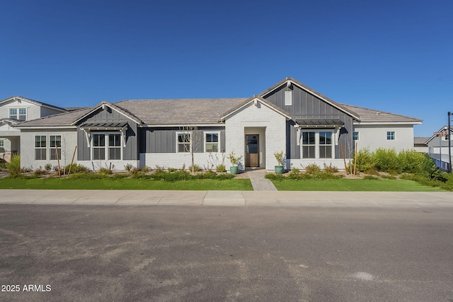 view of front of house featuring a standing seam roof, a front yard, board and batten siding, and brick siding