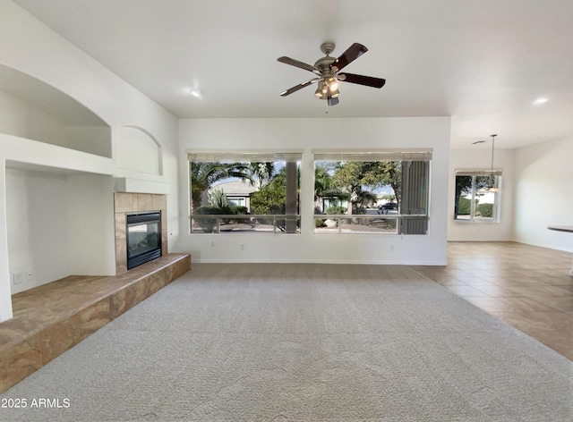 unfurnished living room with ceiling fan, a tiled fireplace, and carpet floors