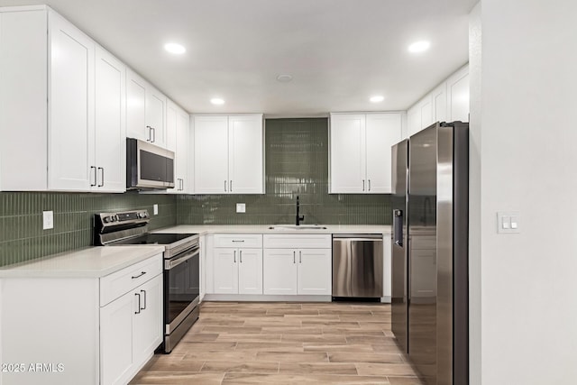 kitchen with appliances with stainless steel finishes, light wood-type flooring, sink, white cabinetry, and backsplash