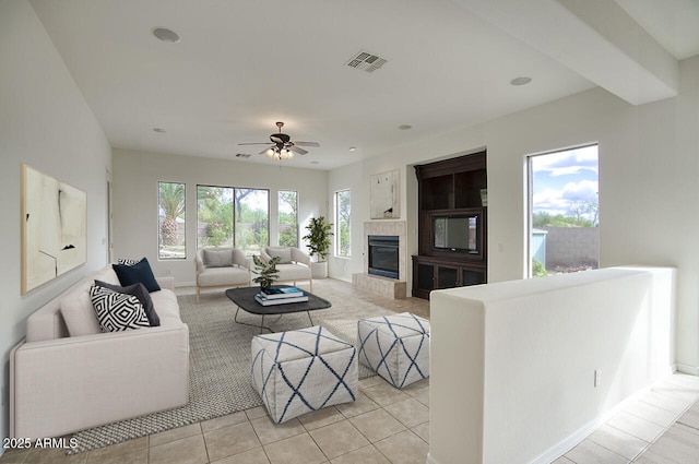 living area with visible vents, a tiled fireplace, light tile patterned flooring, baseboards, and ceiling fan