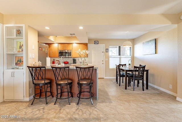 kitchen featuring a breakfast bar, stainless steel appliances, visible vents, a peninsula, and baseboards