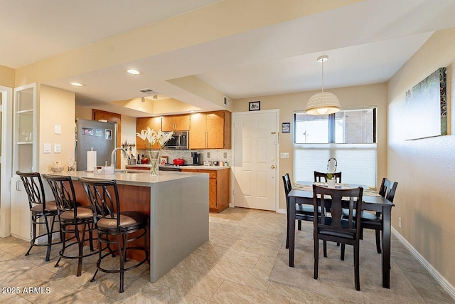 kitchen featuring brown cabinetry, stainless steel microwave, a peninsula, light countertops, and fridge