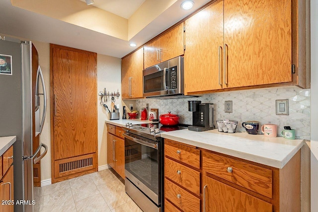 kitchen featuring brown cabinets, stainless steel appliances, light countertops, visible vents, and decorative backsplash