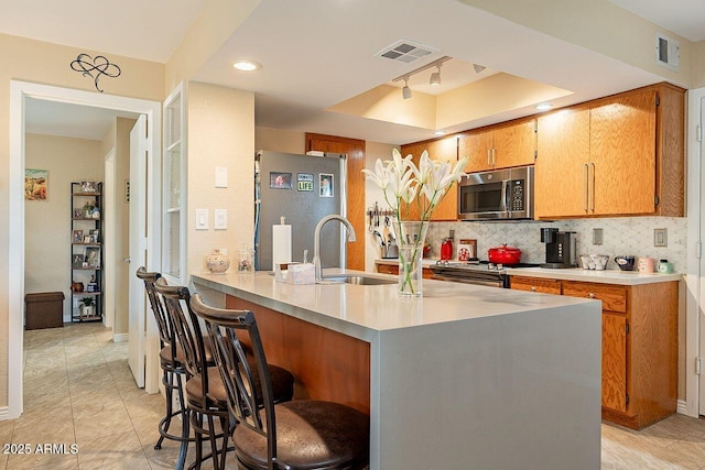 kitchen with visible vents, a breakfast bar area, a sink, stainless steel appliances, and backsplash