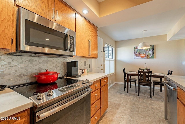 kitchen with baseboards, light countertops, appliances with stainless steel finishes, backsplash, and brown cabinets