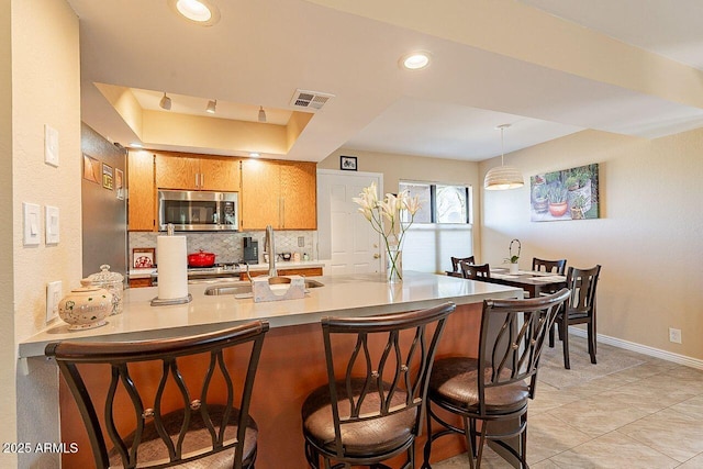 kitchen with stainless steel microwave, visible vents, decorative backsplash, a sink, and a peninsula