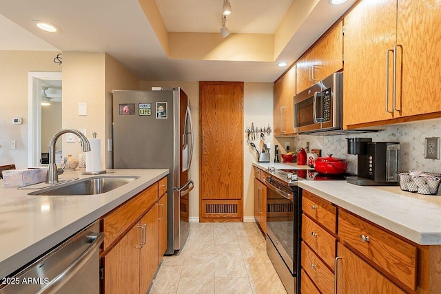 kitchen with a tray ceiling, appliances with stainless steel finishes, brown cabinetry, and a sink