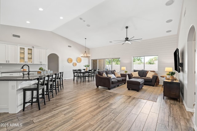 living room featuring arched walkways, a ceiling fan, wood finished floors, lofted ceiling, and visible vents