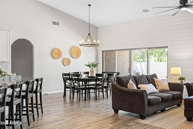 living room featuring visible vents, arched walkways, wood finished floors, high vaulted ceiling, and ceiling fan with notable chandelier