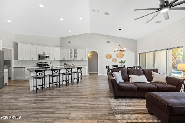 living room with high vaulted ceiling, light wood-type flooring, recessed lighting, arched walkways, and ceiling fan with notable chandelier