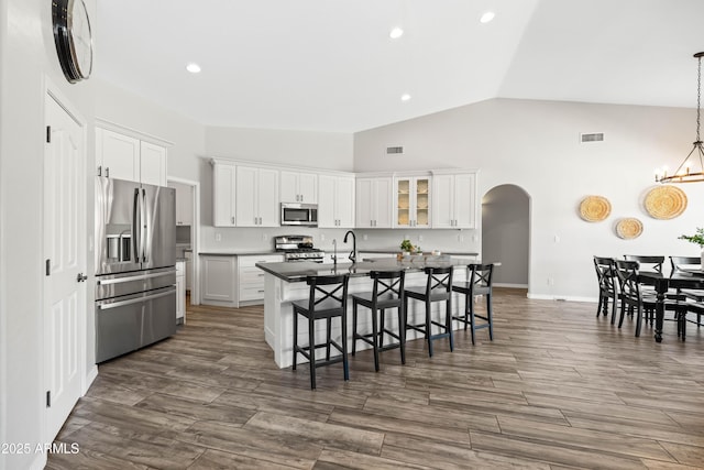 kitchen featuring white cabinets, arched walkways, a kitchen breakfast bar, an island with sink, and stainless steel appliances