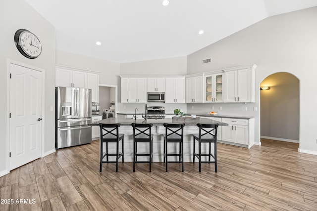 kitchen with a breakfast bar area, arched walkways, a center island with sink, white cabinets, and stainless steel appliances