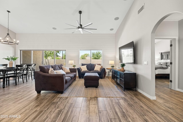 living room featuring a high ceiling, arched walkways, ceiling fan with notable chandelier, wood finished floors, and visible vents