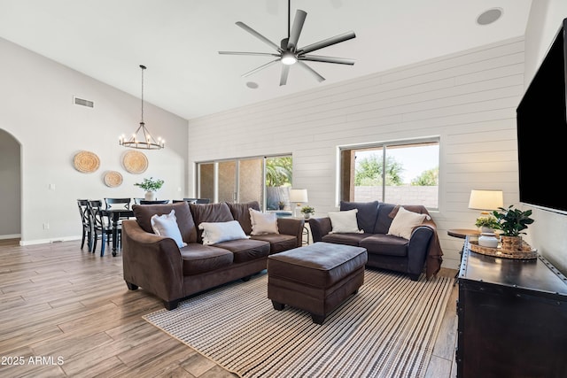 living room featuring visible vents, arched walkways, wood finished floors, high vaulted ceiling, and ceiling fan with notable chandelier