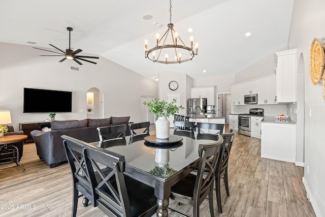dining space featuring arched walkways, light wood finished floors, ceiling fan with notable chandelier, and lofted ceiling