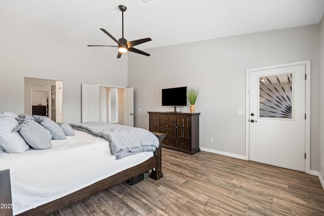 bedroom with baseboards, ensuite bathroom, wood finished floors, and high vaulted ceiling
