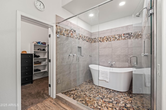 full bath with recessed lighting, a freestanding tub, wood finished floors, a spacious closet, and a stall shower