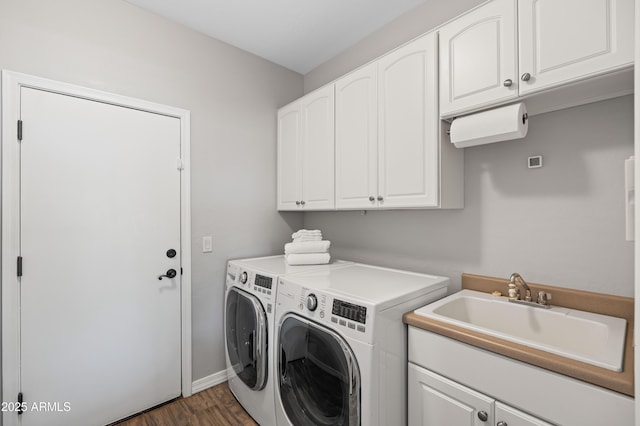 washroom featuring wood finished floors, baseboards, washer and clothes dryer, a sink, and cabinet space