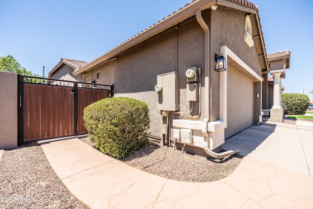 view of side of property with a gate, stucco siding, a tile roof, and concrete driveway