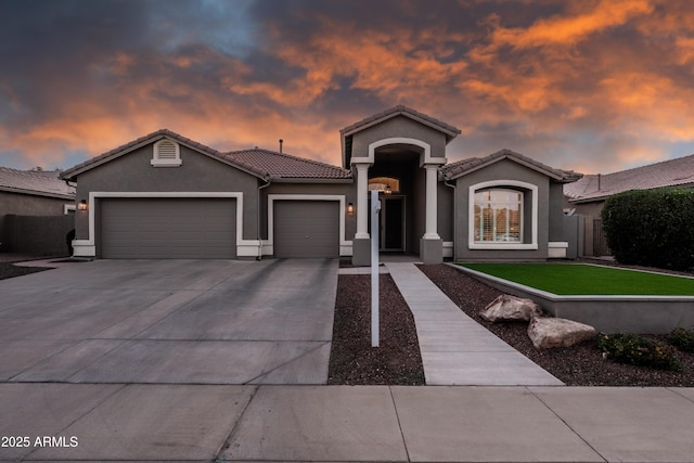 view of front facade with fence, a tile roof, a garage, stucco siding, and concrete driveway