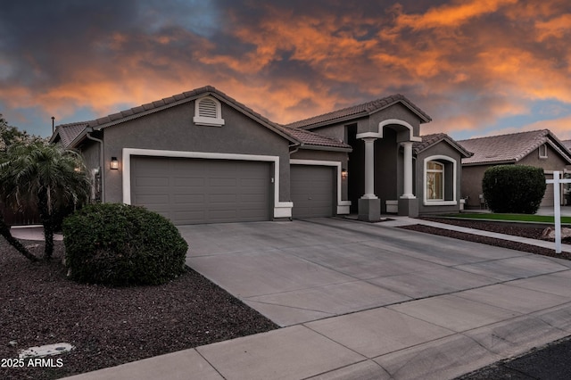 mediterranean / spanish house featuring a tiled roof, a garage, stucco siding, and driveway