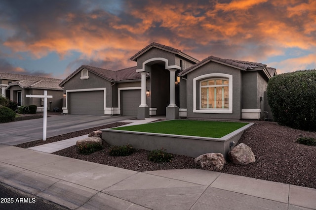 mediterranean / spanish-style home with a lawn, stucco siding, a tiled roof, concrete driveway, and an attached garage