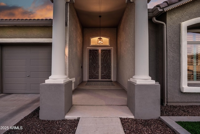 exterior entry at dusk with an attached garage, a tile roof, and stucco siding