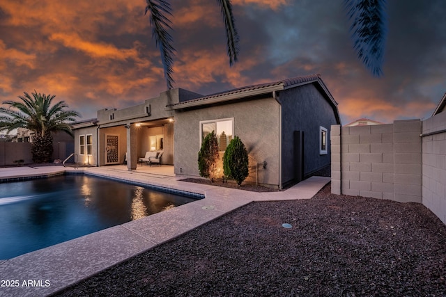 back of property at dusk with stucco siding, fence, a patio area, and a fenced in pool