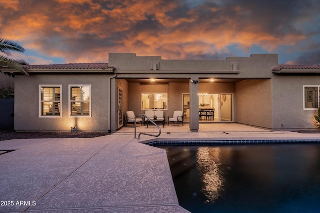 rear view of house with a patio, stucco siding, a tile roof, and an outdoor pool