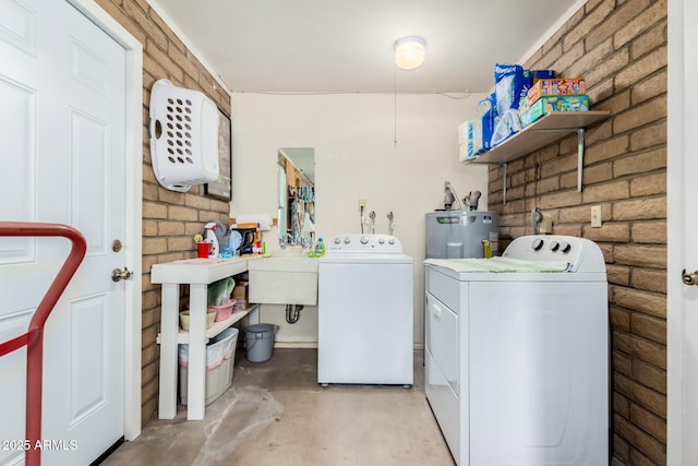 laundry area with electric water heater, sink, independent washer and dryer, and brick wall