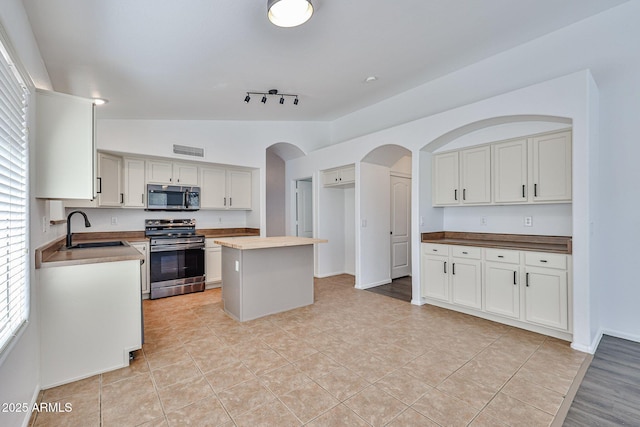 kitchen with visible vents, a sink, stainless steel appliances, vaulted ceiling, and a center island