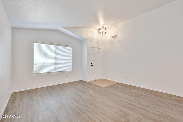 empty room with light wood finished floors, visible vents, baseboards, vaulted ceiling, and a textured ceiling