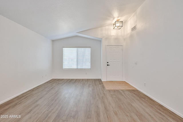 entrance foyer with baseboards, visible vents, lofted ceiling, light wood-style floors, and a textured ceiling