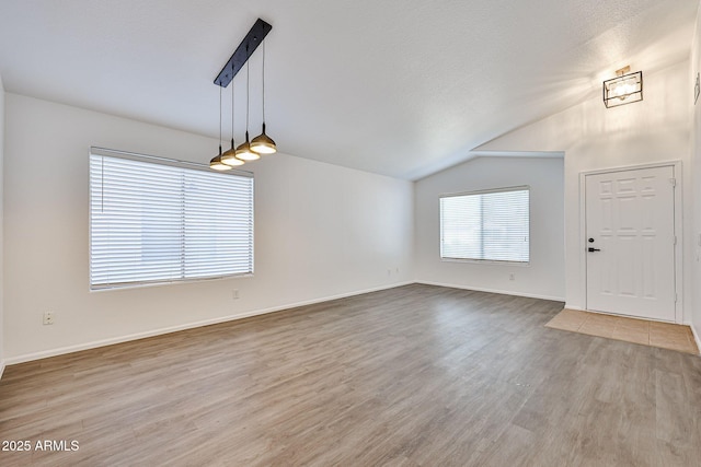 interior space with baseboards, a textured ceiling, wood finished floors, and vaulted ceiling