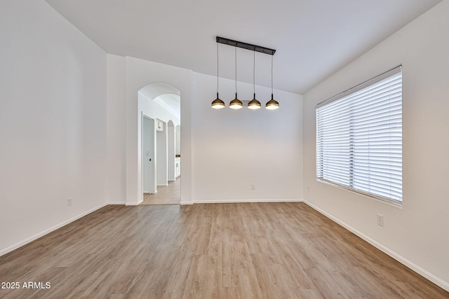 unfurnished room with baseboards, arched walkways, and light wood-style floors