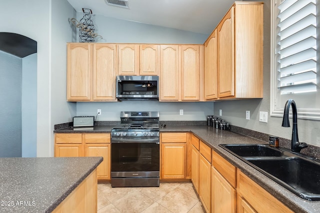 kitchen with dark countertops, light brown cabinets, a sink, and appliances with stainless steel finishes