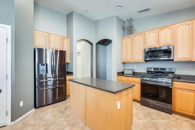 kitchen with a center island, appliances with stainless steel finishes, light brown cabinets, and dark countertops