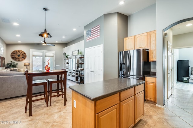 kitchen with ceiling fan, arched walkways, dark countertops, stainless steel fridge, and open floor plan
